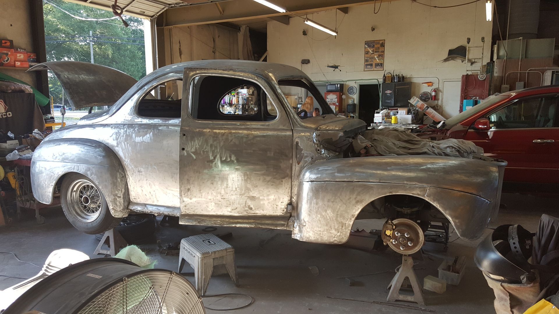 A silver car is sitting in a garage with the hood up.