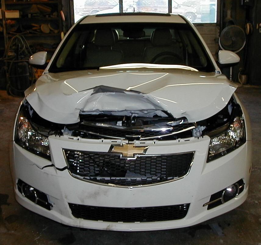 A white chevrolet with a damaged hood is parked in a garage
