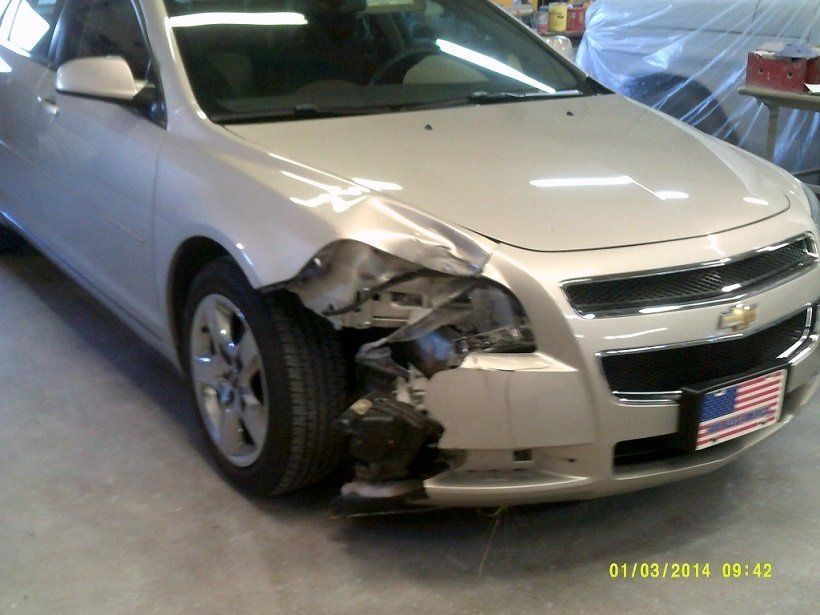 A silver car with a damaged front end is parked in a garage