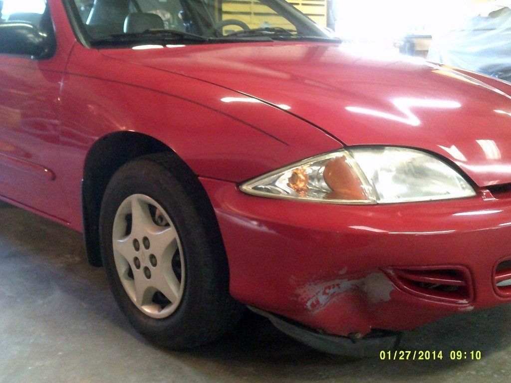 A red car with a damaged front bumper is parked in a garage
