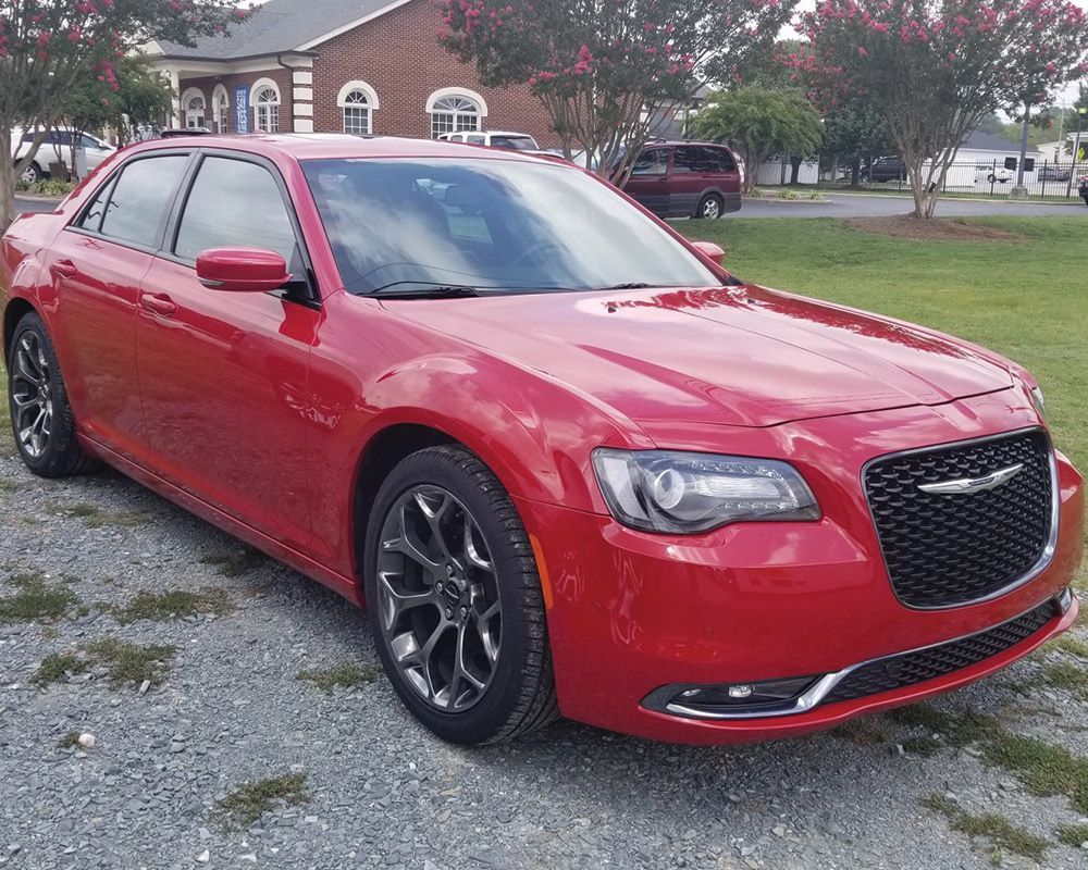 A red chrysler 300 is parked in front of a house.