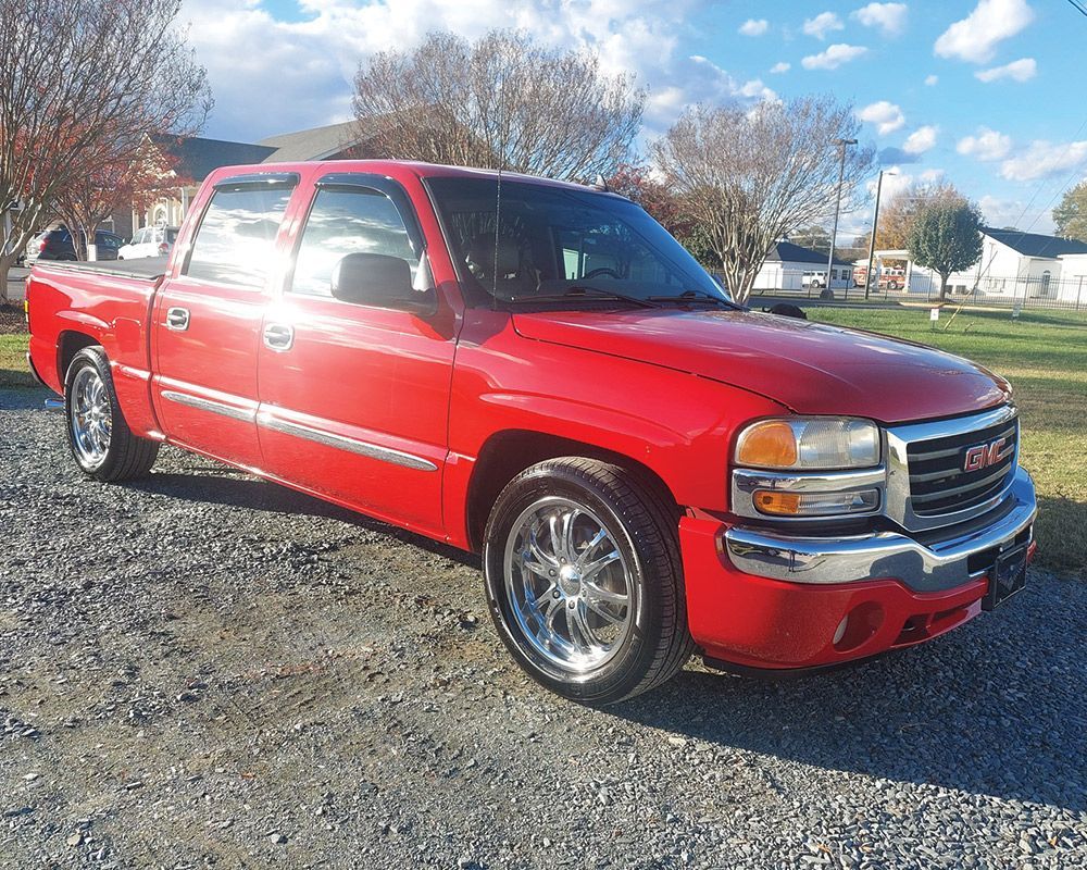 A red gmc truck is parked on a gravel road.