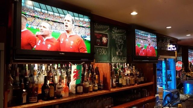 A sports bar with a lot of bottles on the shelves and two televisions on the wall.