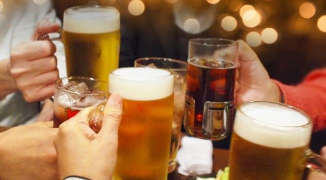 ビールを含む様々な飲み物を片手に乾杯する人々。背景にはぼんやりとした温かみのある光が灯っている。
