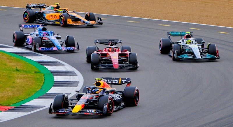 A group of F1 race cars are racing on a race track.