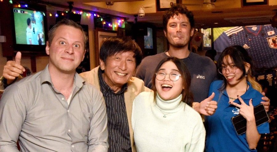 A group of people from several different nations are posing for a picture in a sports bar in Nagoya, Japan.