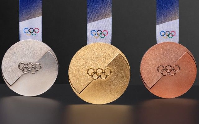 Three Olympic medals: silver, gold, and bronze, with the Olympic rings and blue ribbons against a dark background.