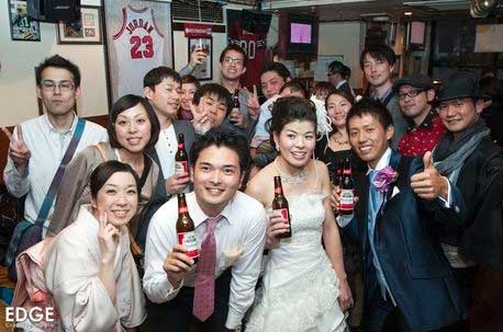 新郎新婦がビールボトルを持ちながら、グループの人々と一緒に写真を撮っているシーン