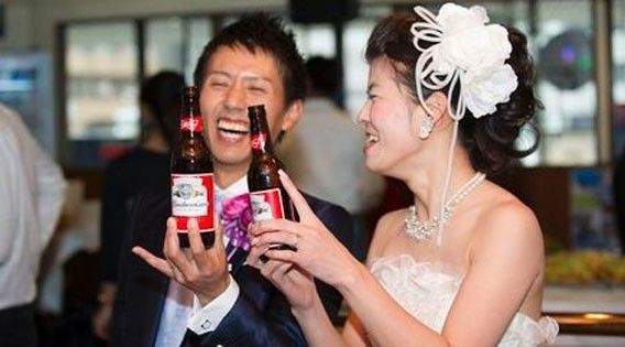 A bride and groom are holding bottles of beer in their hands.