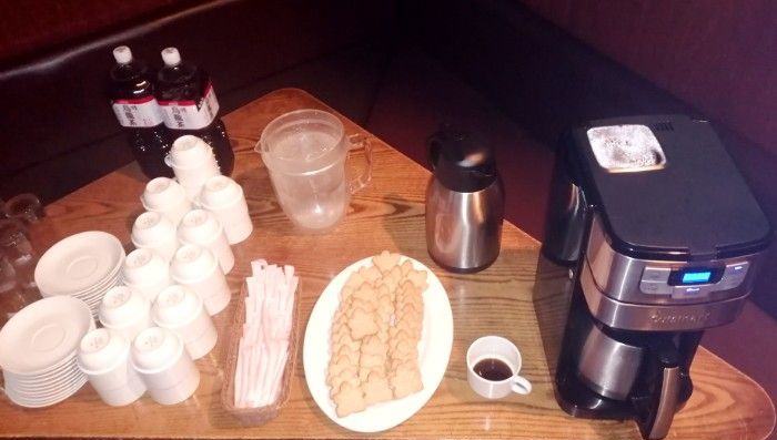 A table with a coffee maker and a plate of cookies on it, arranged for a seminar.