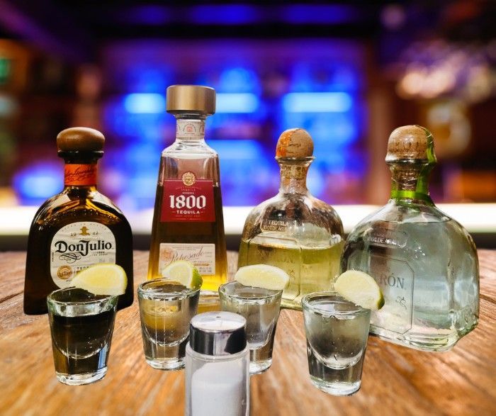 Shots of tequila in front of 4 bottles of tequila on a bar counter