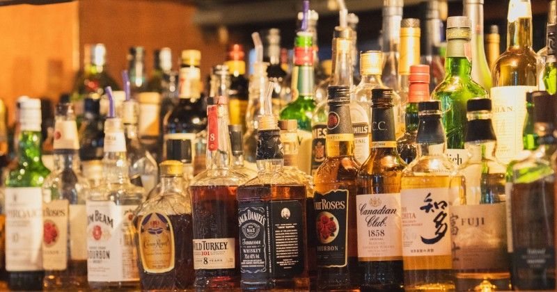Whisky bottles displayed on a wooden shelf, illuminated by soft lighting at a Nagoya sports bar.