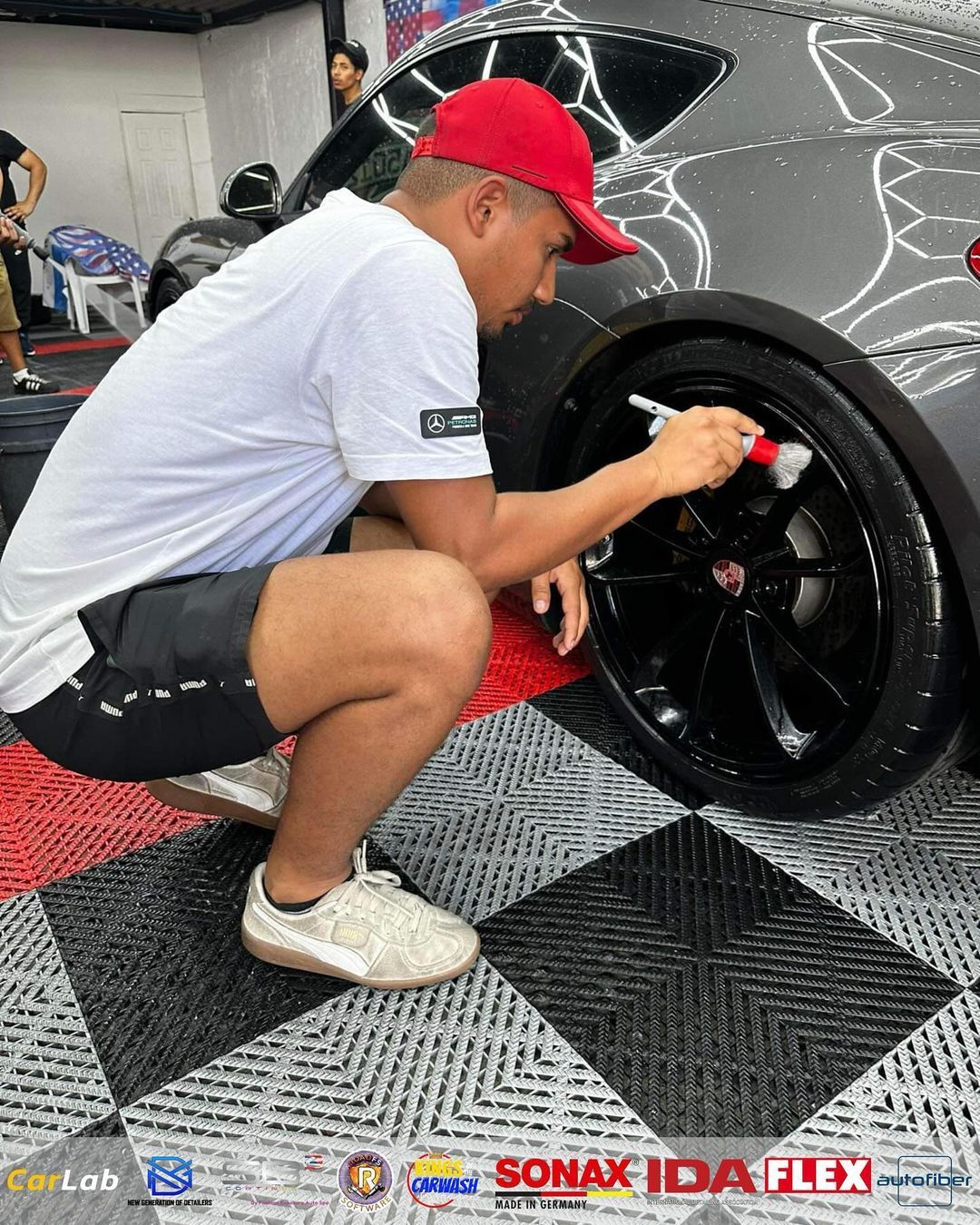 A man is kneeling down and cleaning a car wheel with a brush.