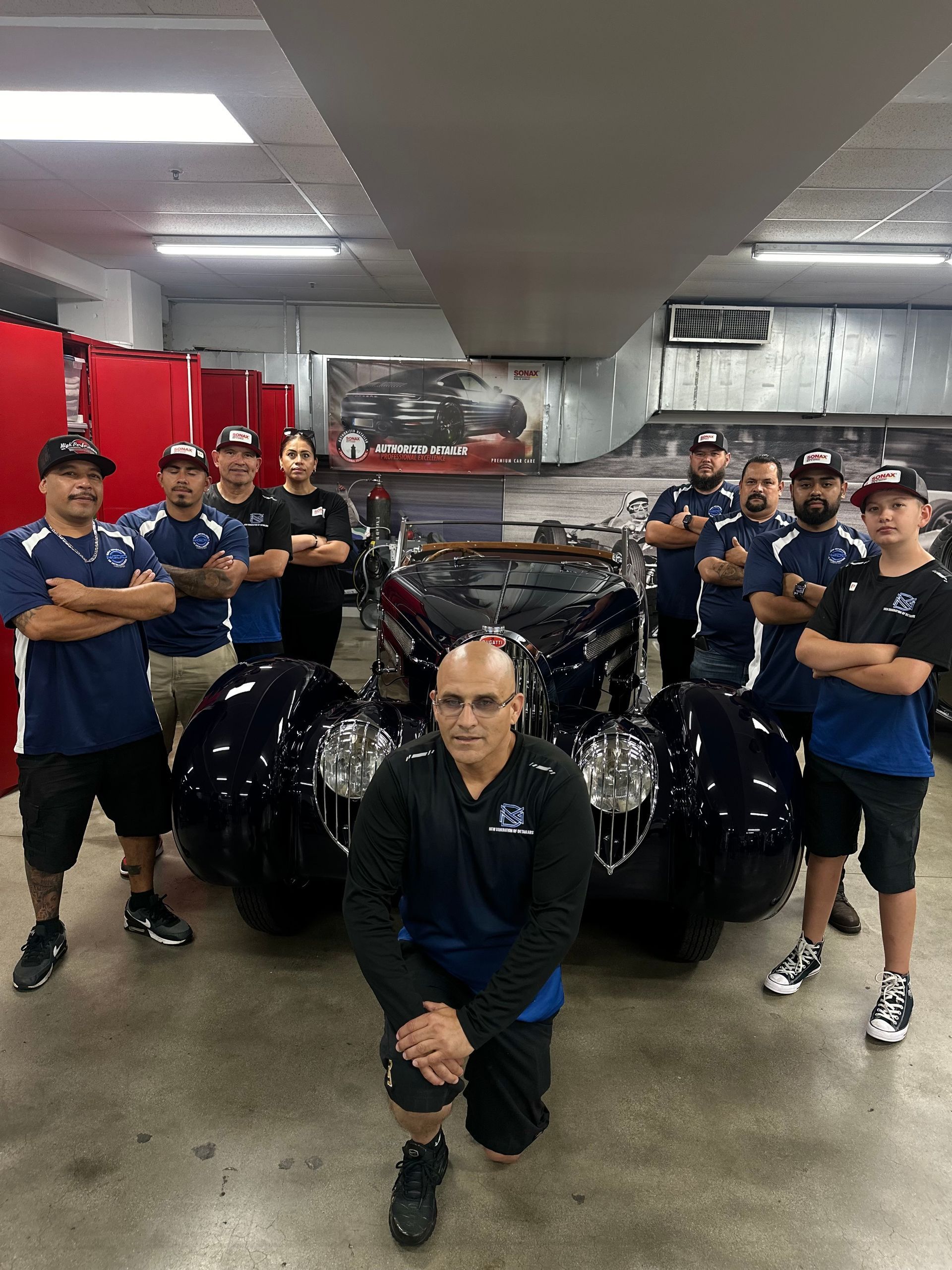 A group of men are posing for a picture in front of a car in a garage.
