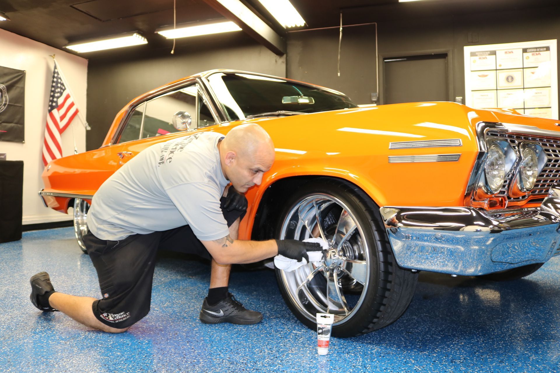 A man is kneeling down next to an orange car in a garage