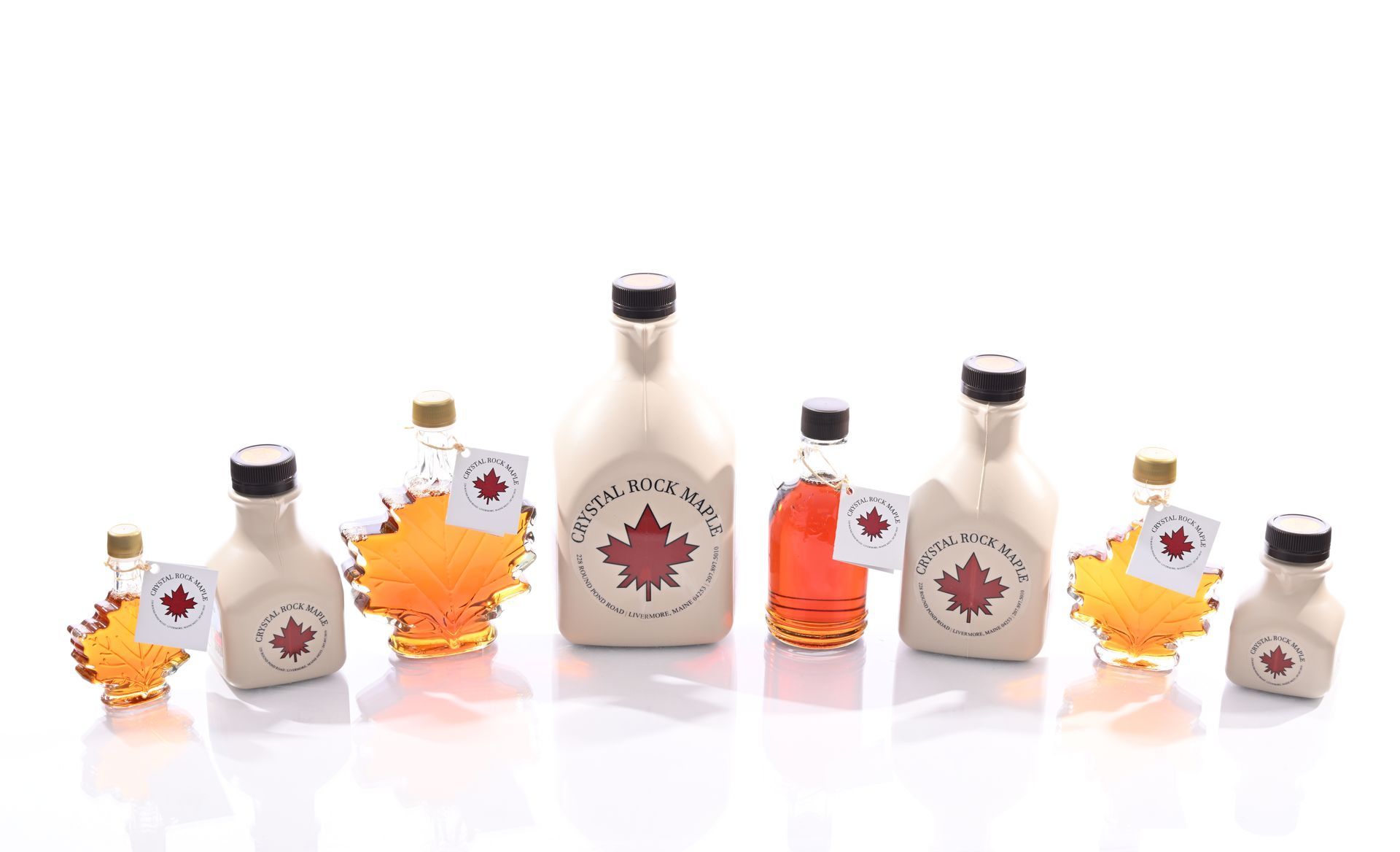 Bottles of maple syrup in various sizes, with a maple leaf logo, arranged on a white surface.