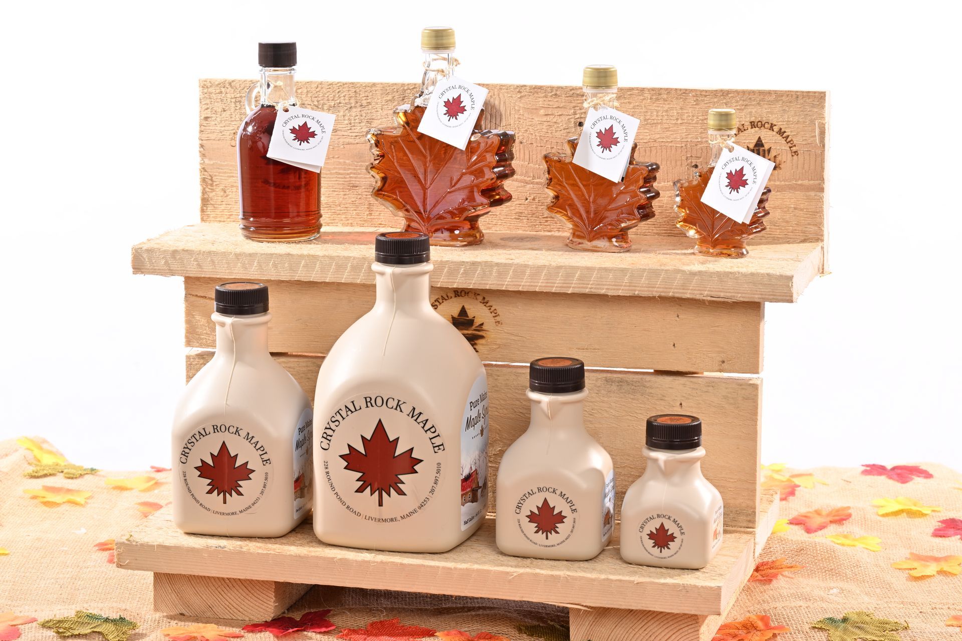 Maple syrup bottles in various sizes on a wooden display; some are maple leaf-shaped.