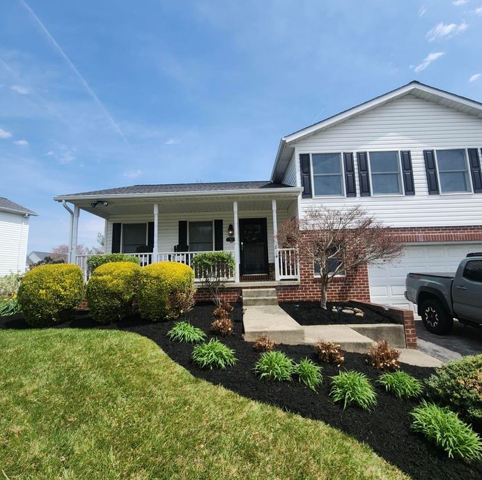 Two-story house with black mulch landscaping, bushes, and a gray truck in driveway under a blue sky.