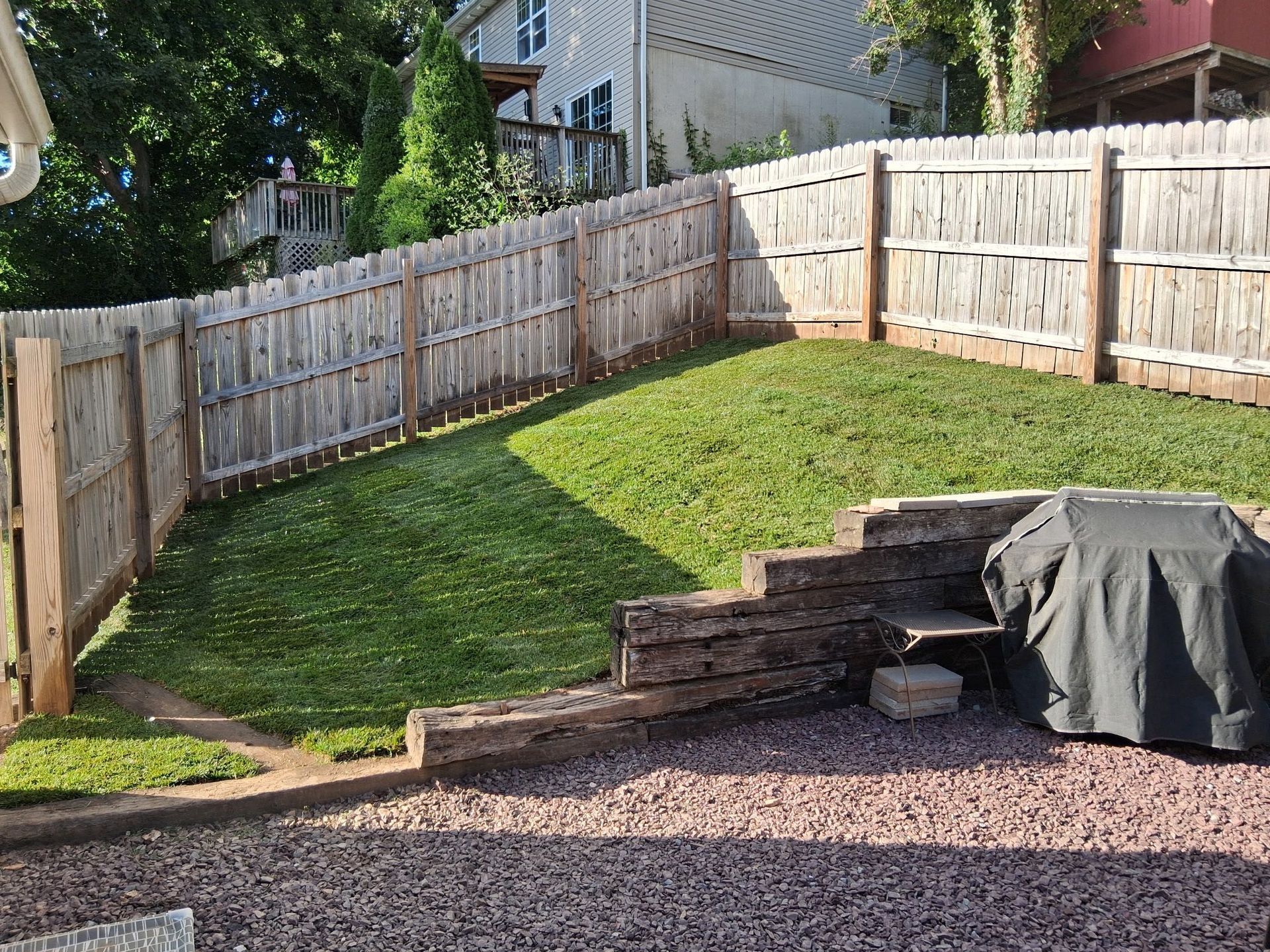 Backyard with grass, wooden fence, steps, and covered grill.