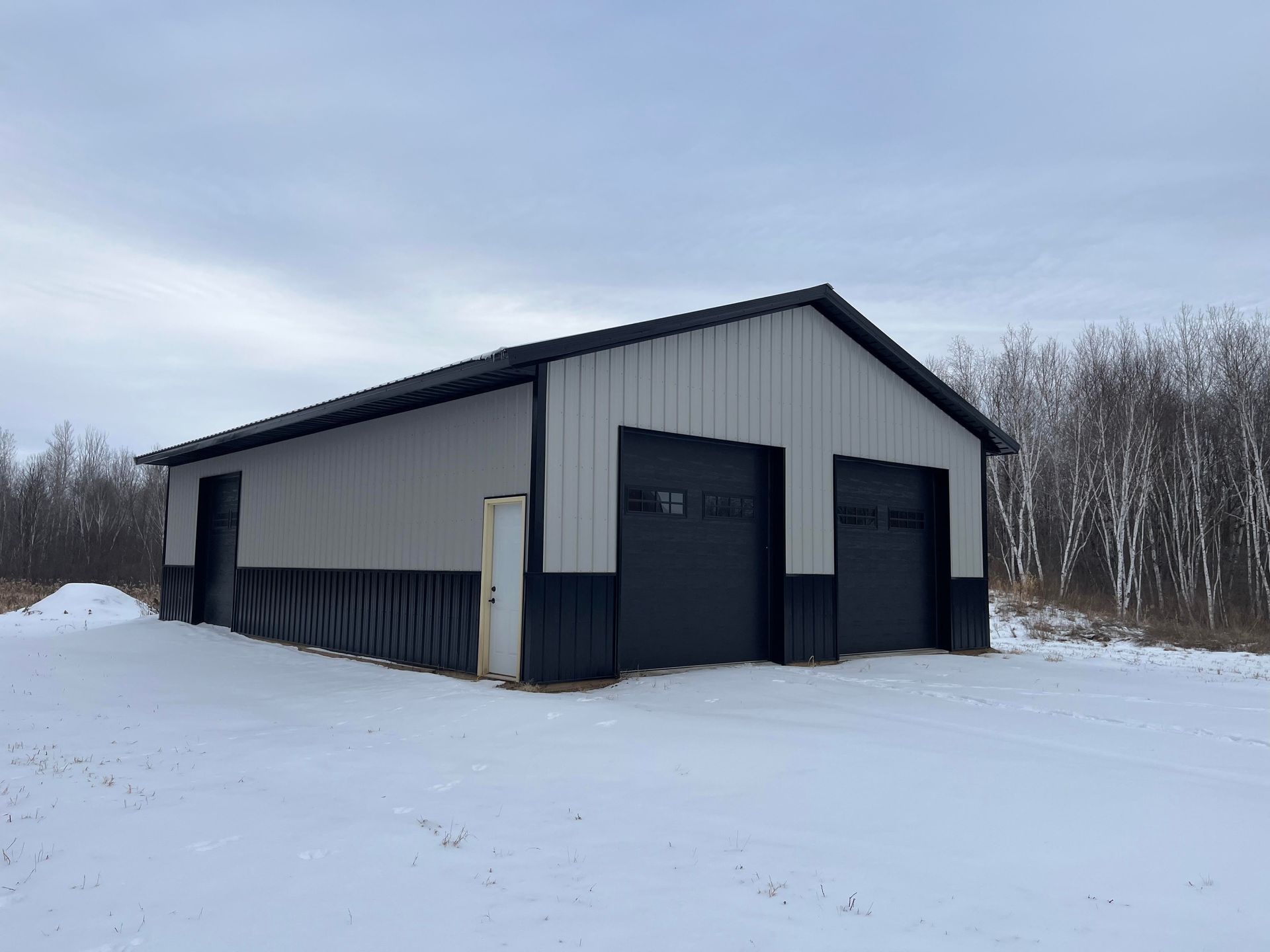 A black and white garage is sitting in the middle of a snow covered field.