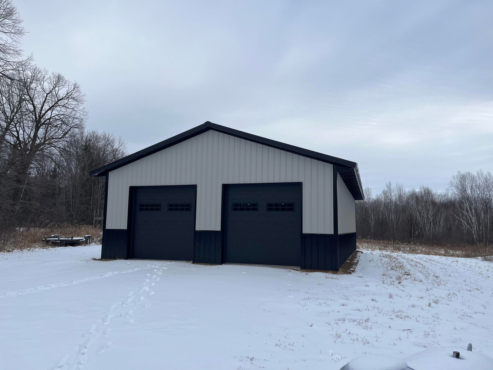 A white and black garage with two garage doors in the snow.