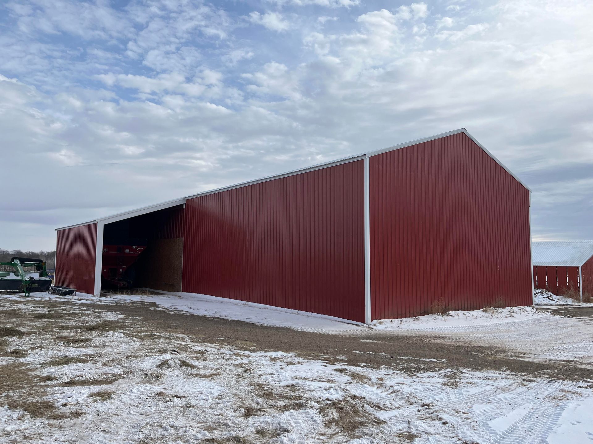 A large red barn is sitting in the middle of a snowy field.