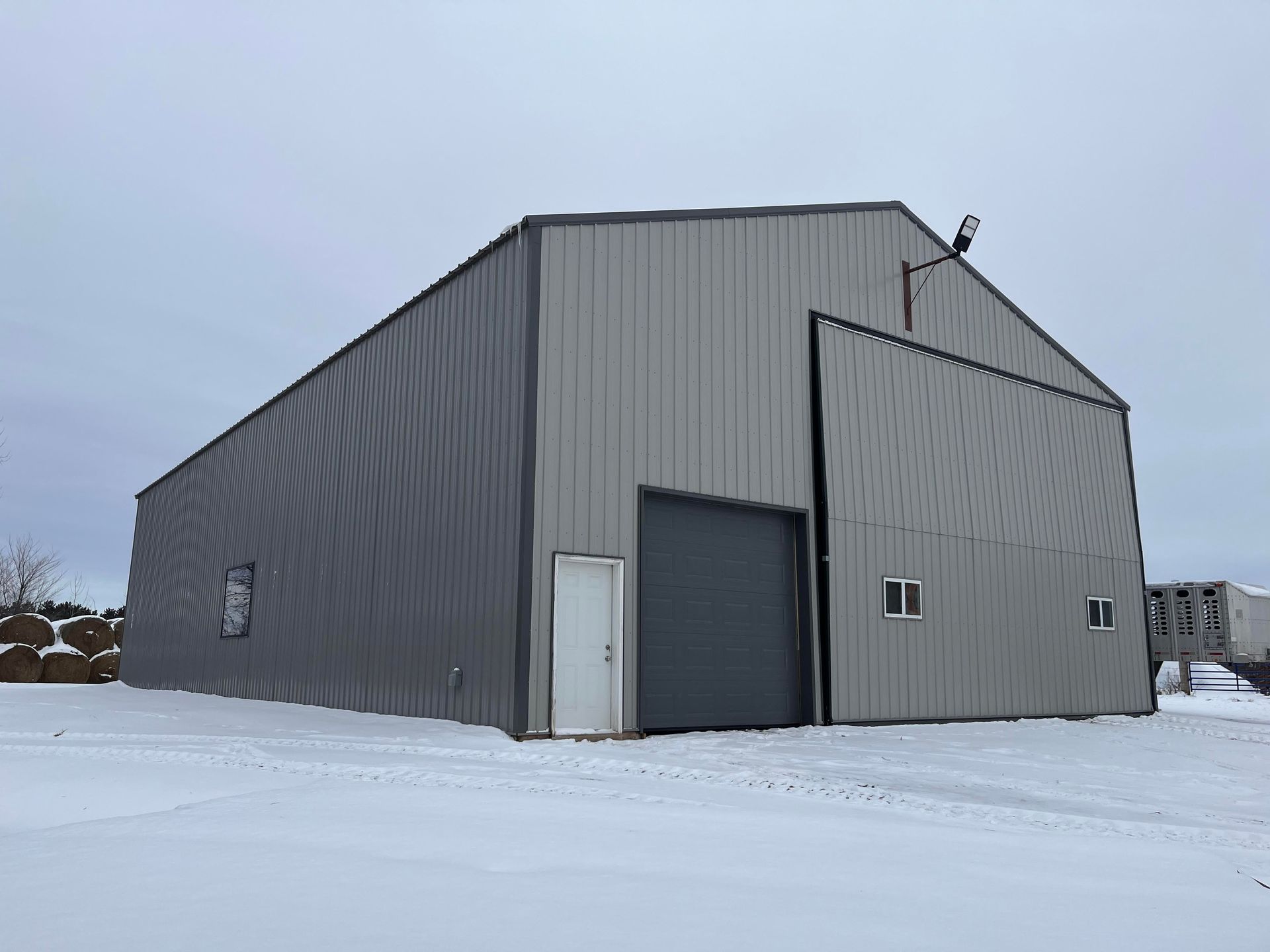A large metal building with a large garage door is covered in snow.