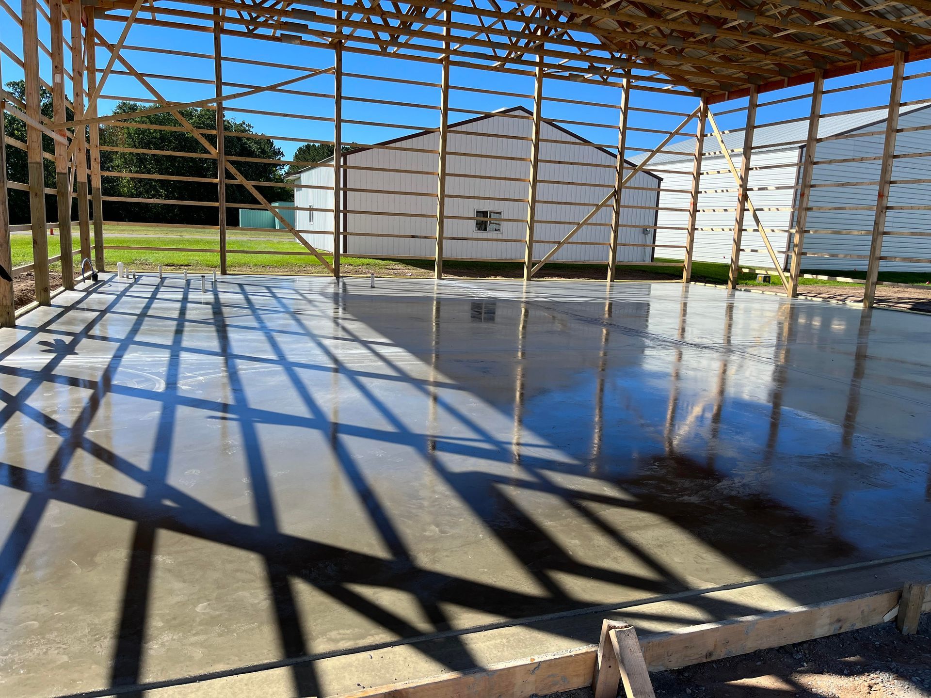 A concrete floor under a wooden structure with a white building in the background.