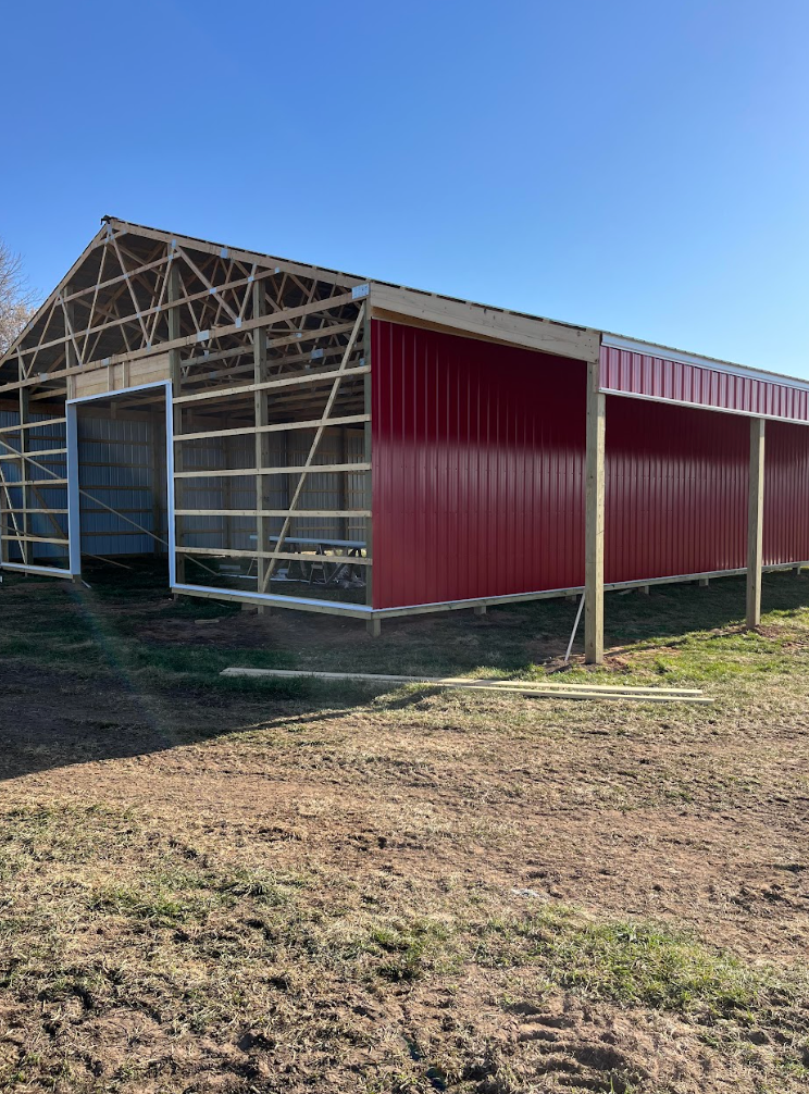 A large red barn is sitting in the middle of a dirt field.