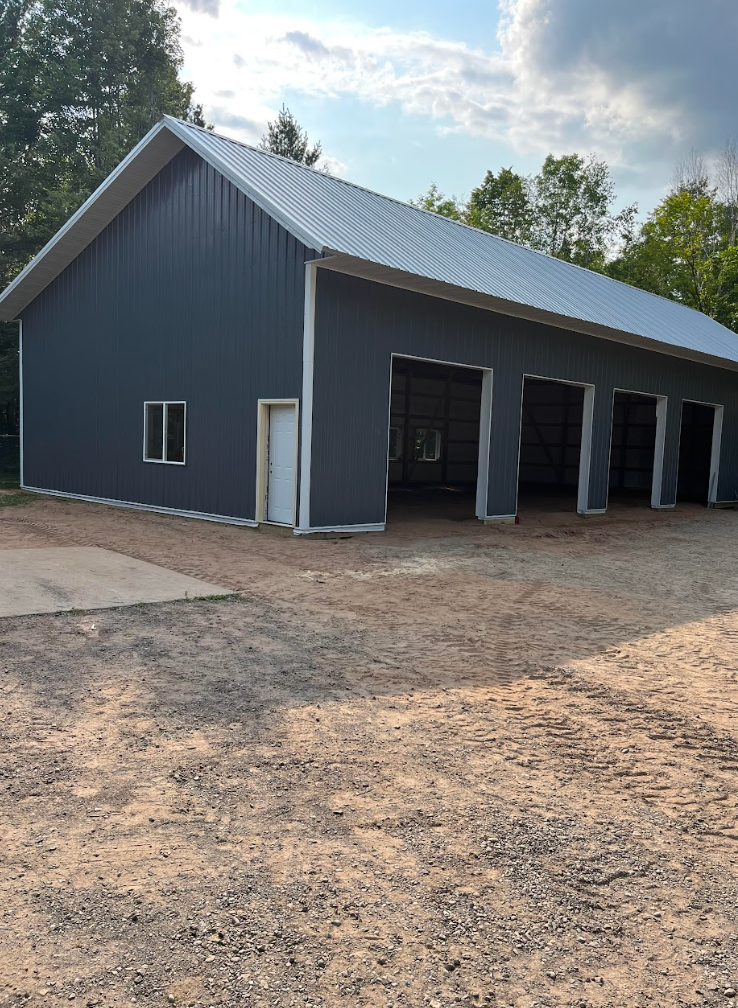 A large gray building with a white roof is sitting in the middle of a dirt field.