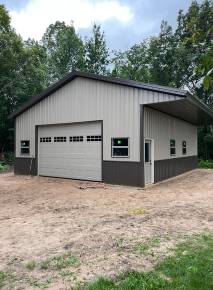 A garage with a large garage door is sitting in the middle of a dirt field.