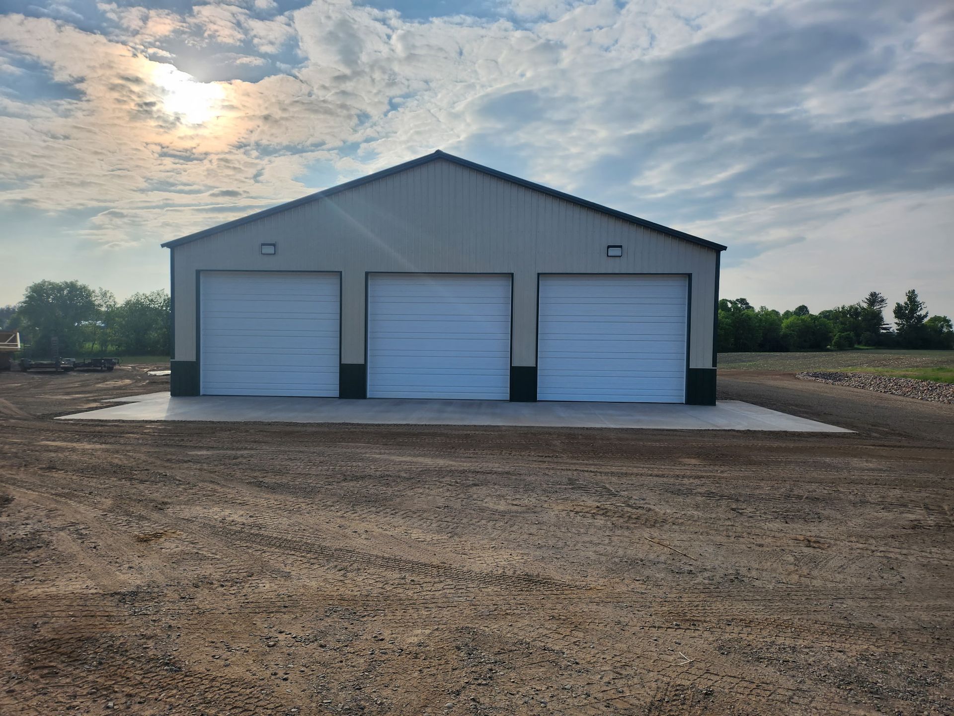 A garage with three white garage doors in a dirt field