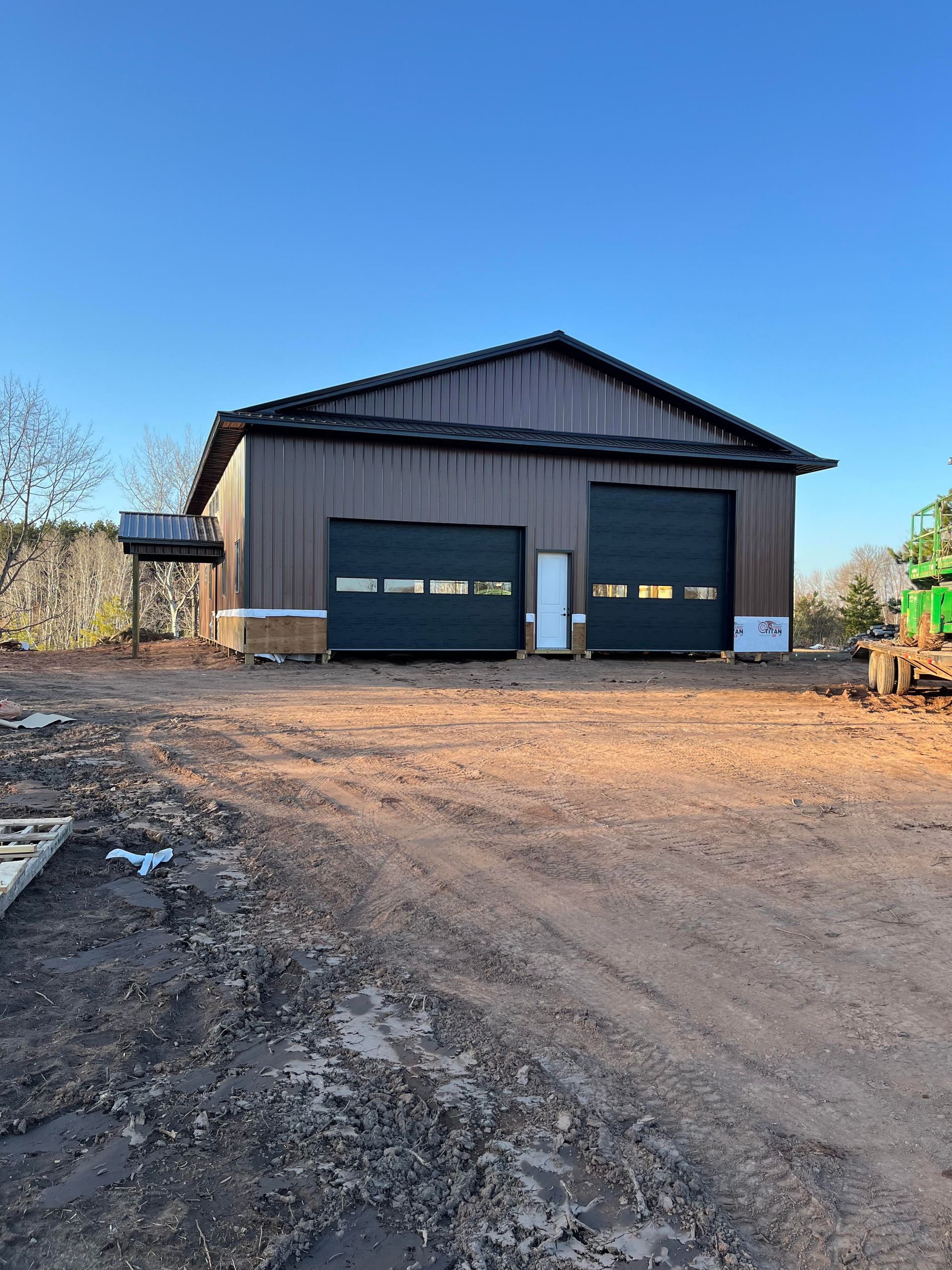 A large barn with two garage doors is sitting on top of a dirt field.