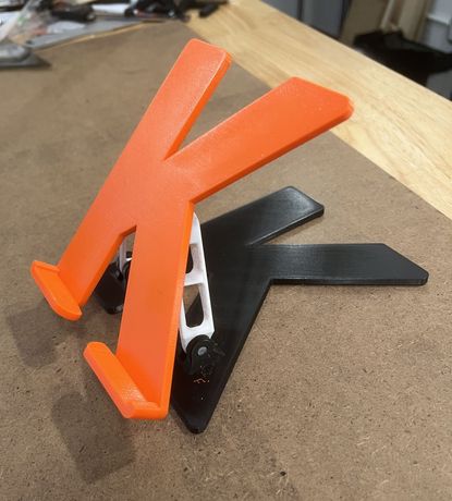 Fully assembled custom 3D printed “K” letter standing on our Brooklyn workshop bench. The vibrant orange front pairs with a sturdy black backplate and white internal brackets — a complete, ready-to-mount piece created through our local 3D printing service in Brooklyn, NY.