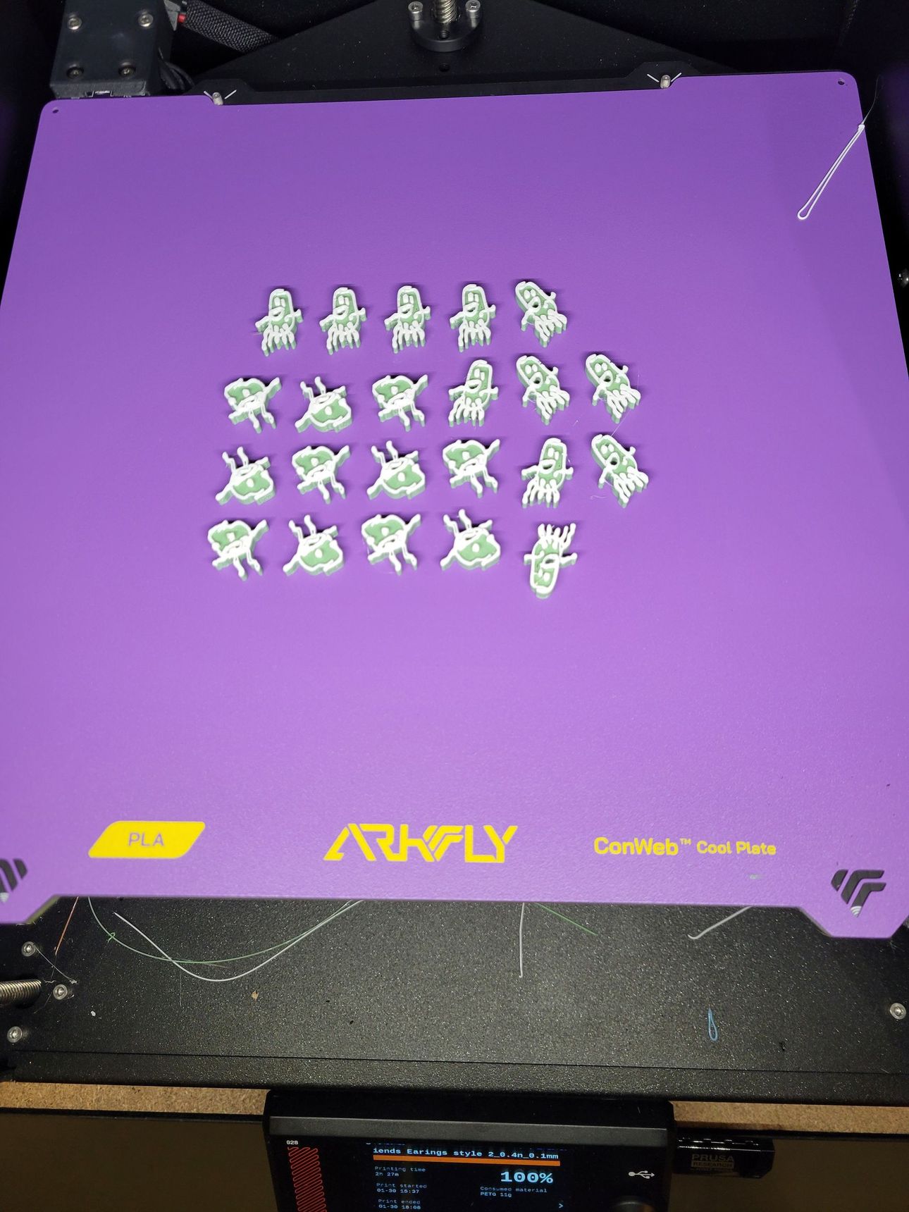 Twenty-one small, white, 3D-printed figures shaped like Plankton from SpongeBob arranged on a purple print bed.