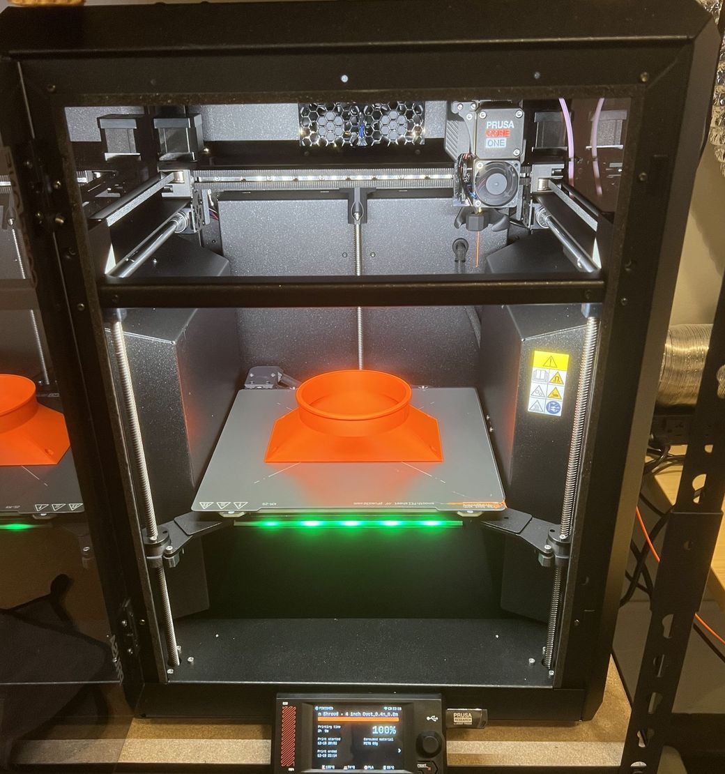 A 3D printer with a black frame, illuminated by internal green lights, actively printing an orange object on the build plate.