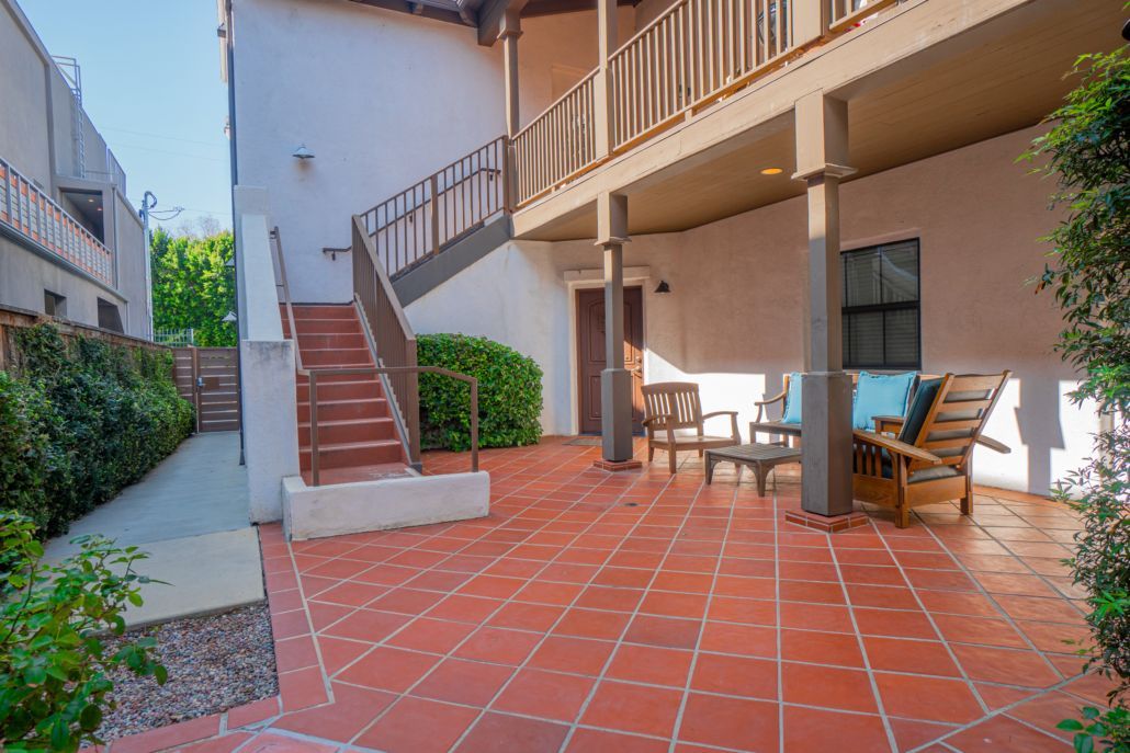 A patio with chairs , tables and stairs in front of a building.