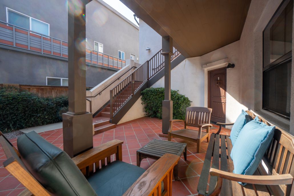 A porch with a couch and chairs and stairs in the background