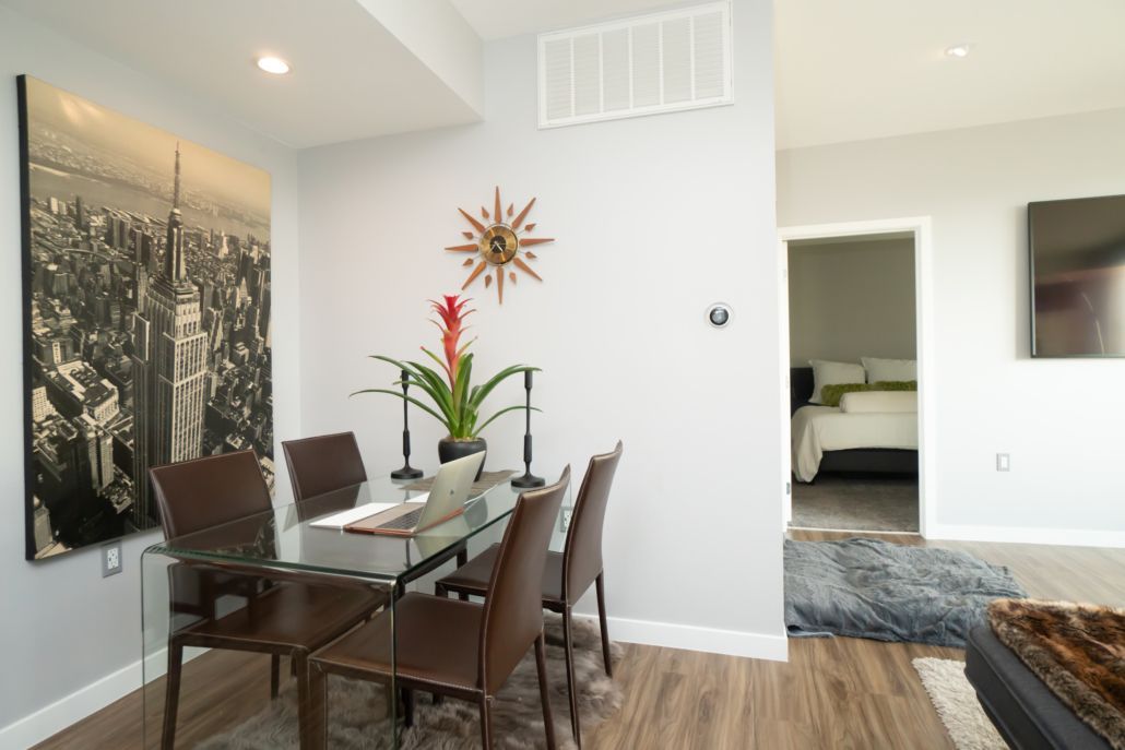 A dining room with a glass table and chairs and a painting on the wall.