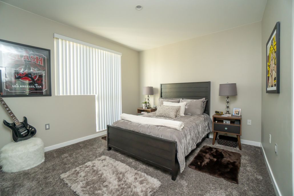 A bedroom with a bed , nightstands , lamps and a guitar on the floor.