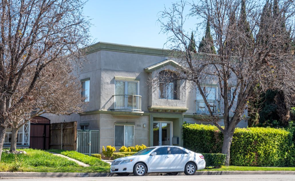 A white car is parked in front of a large house.