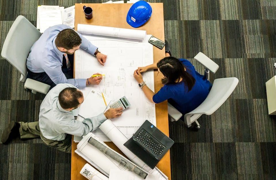 A group of people are sitting around a table looking at blueprints.