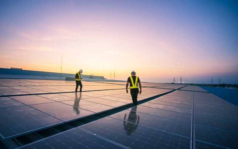 Two workers walking amongst solar panels on a roof