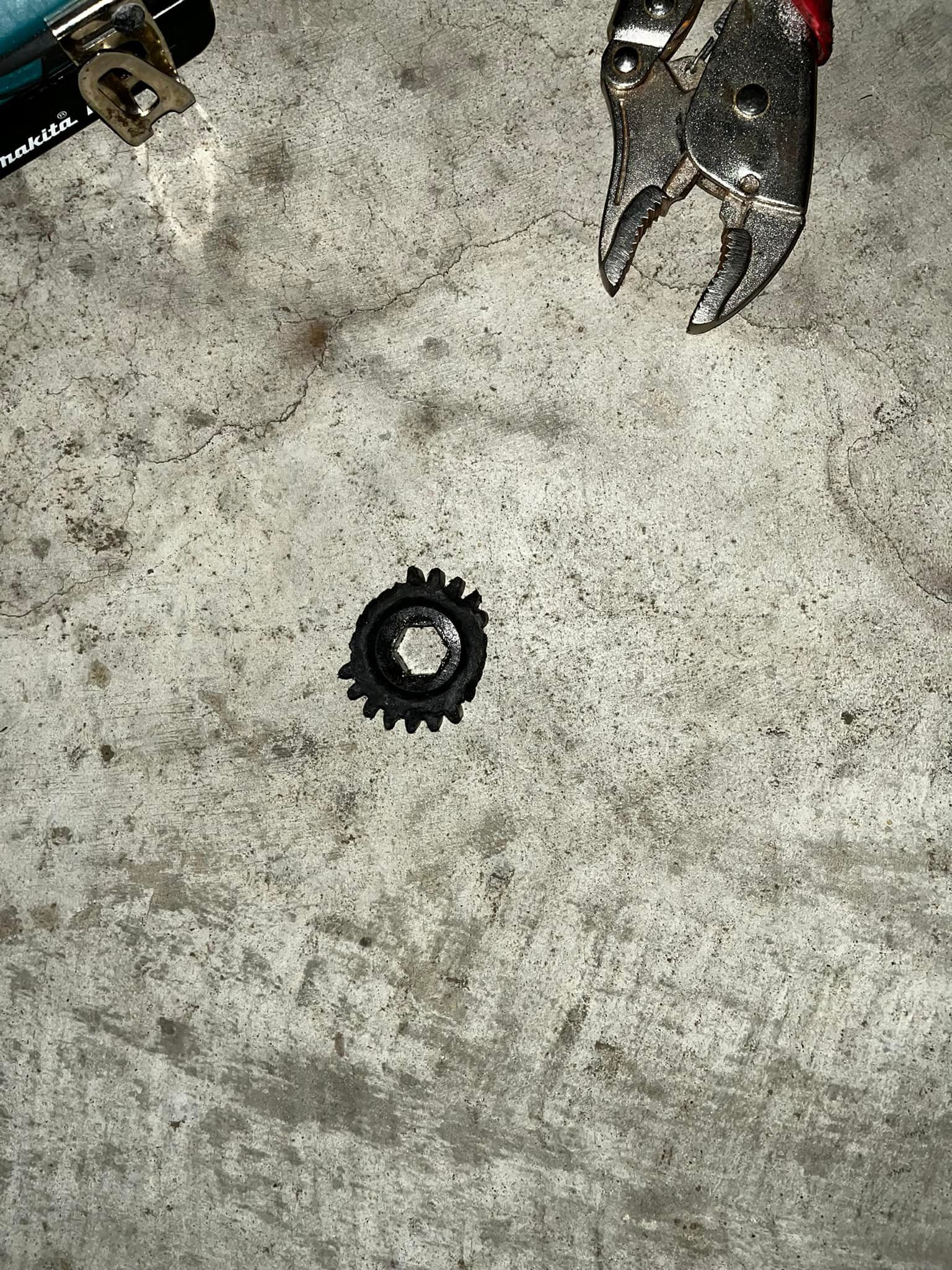 A pair of pliers is being used to remove a gear from the ground.
