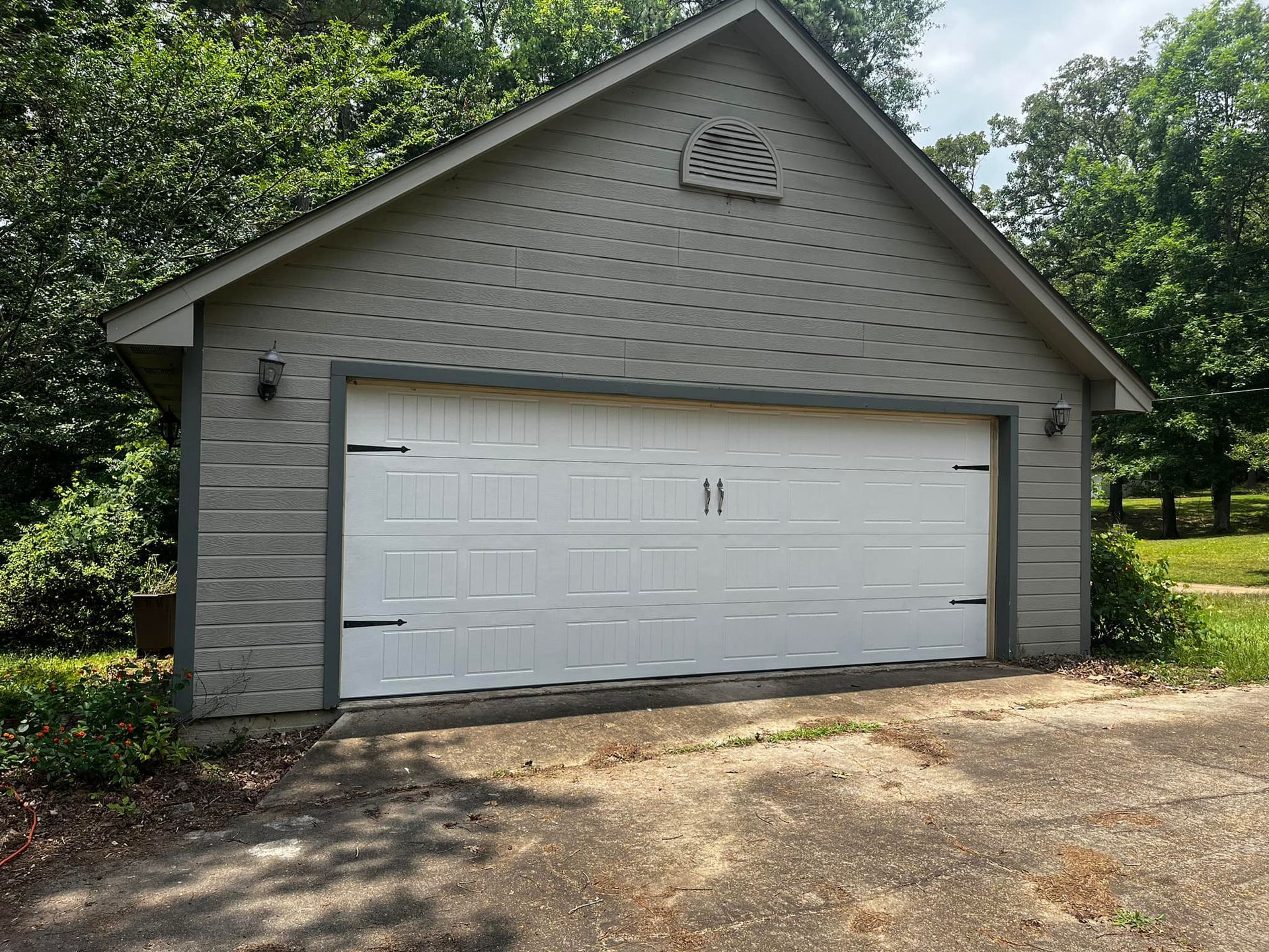 A garage with a white door and a roof surrounded by trees.