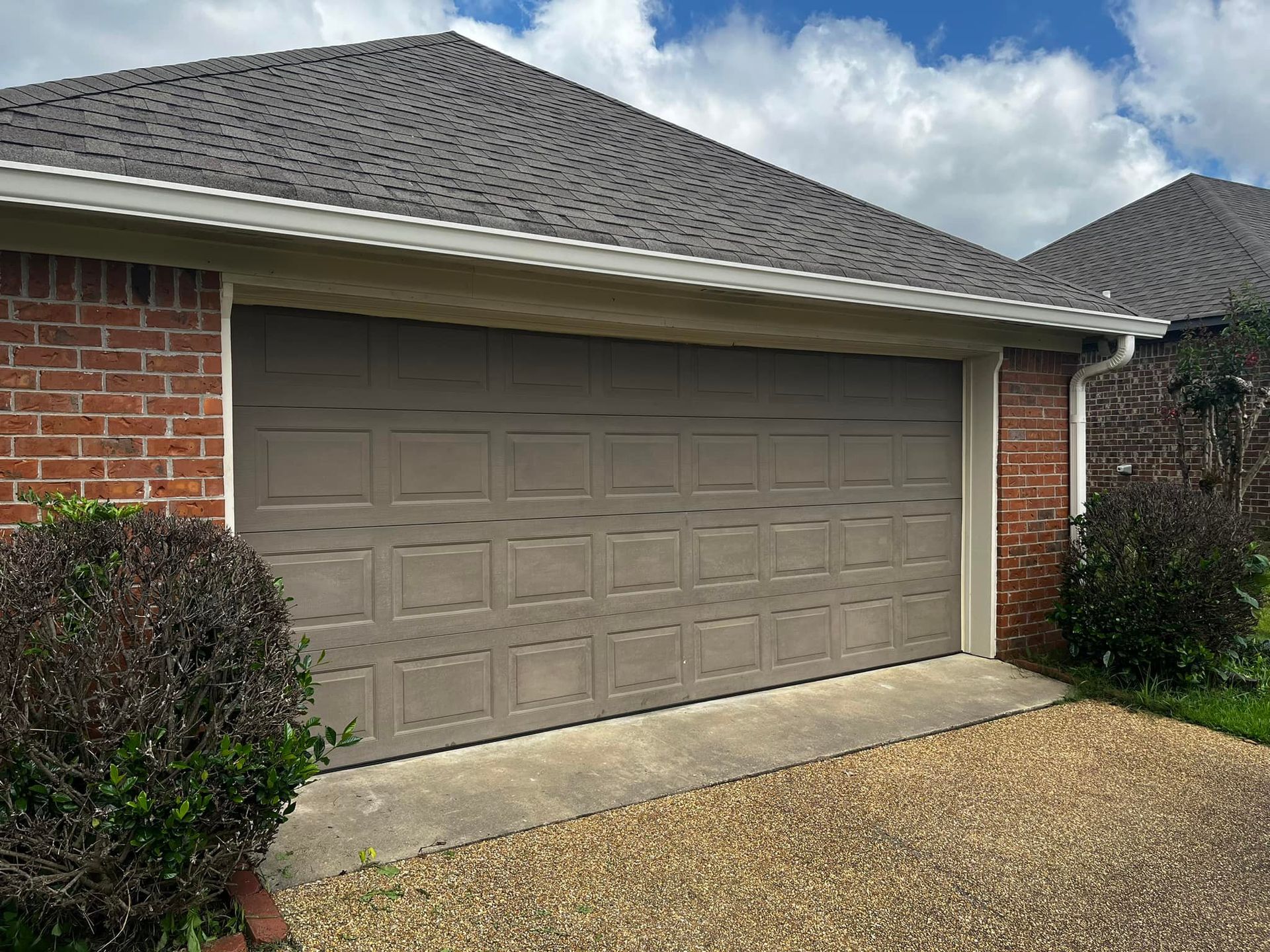 A brick house with a large garage door and a gravel driveway.