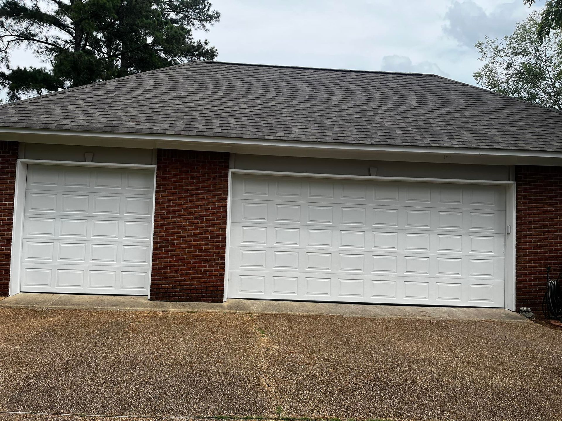 A brick house with two white garage doors and a gray roof.