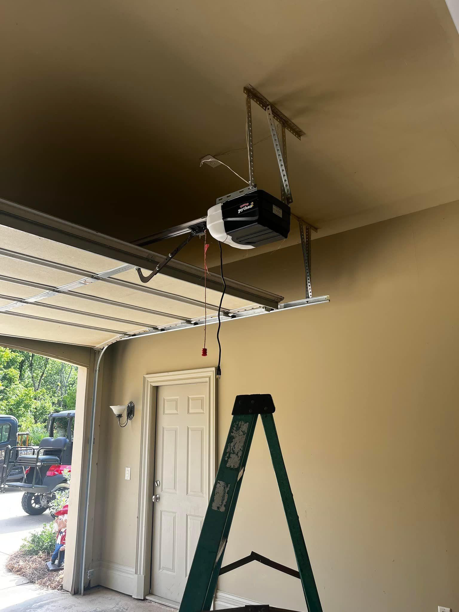A garage door opener is hanging from the ceiling next to a ladder.