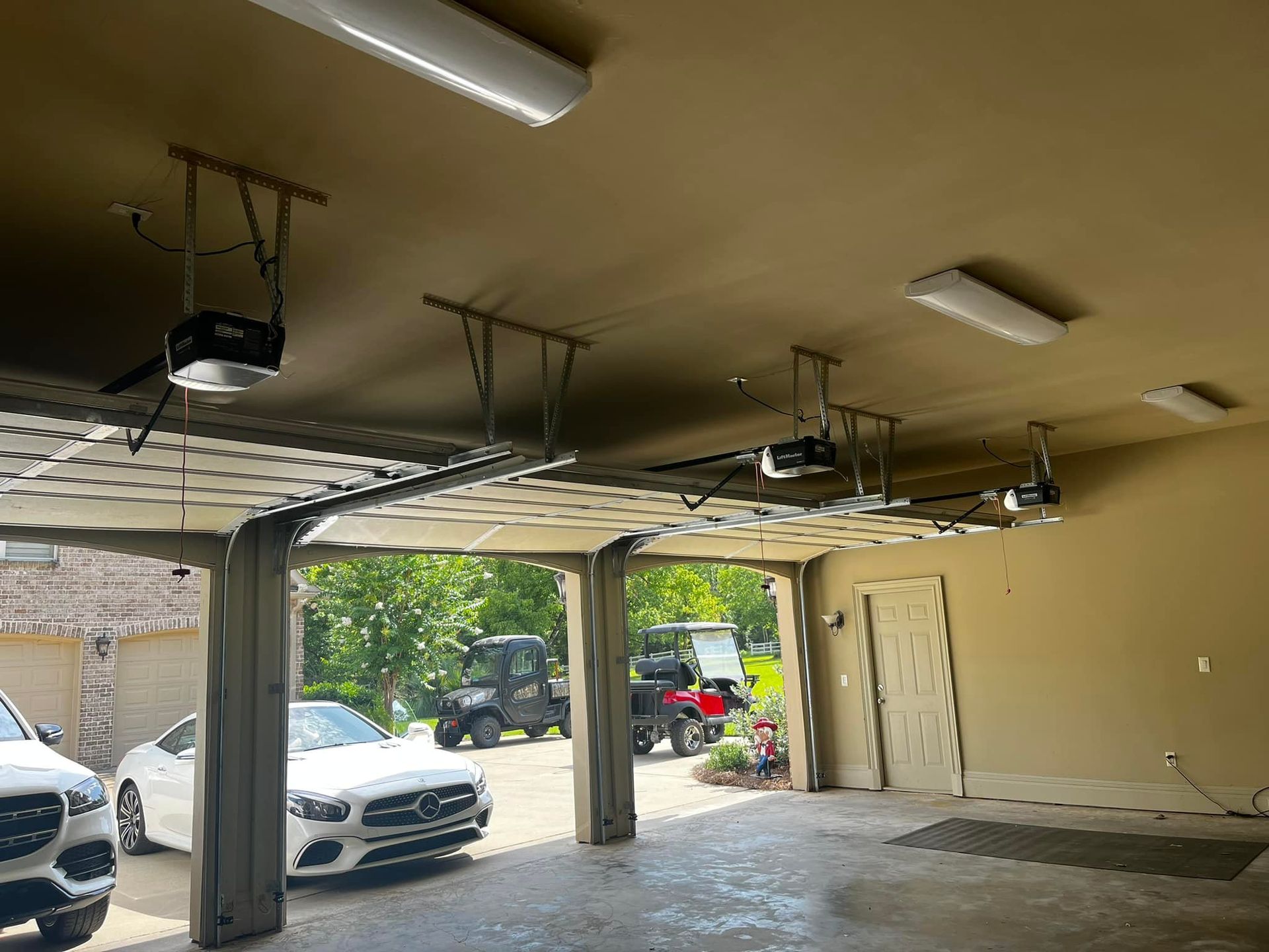 Two cars are parked in a garage with a garage door open.