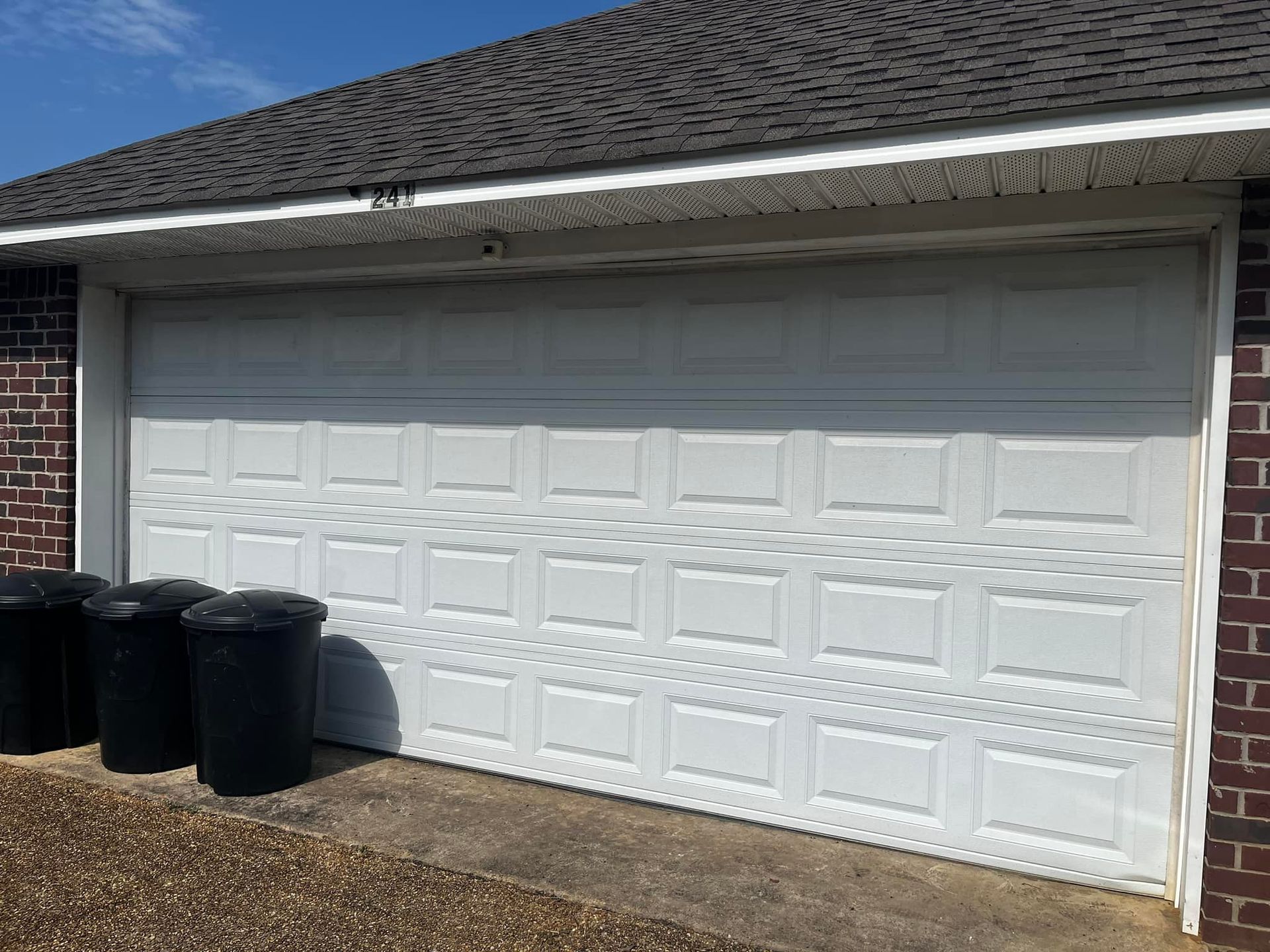 A white garage door is sitting in front of a brick house.
